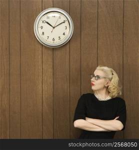 Mid-adult Caucasian female in vintage outfit looking up at clock.