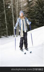 Mid adult Caucasian female skier wearing blue ski clothing standing on ski slope smiling.