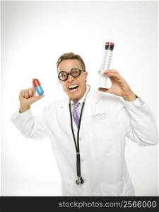 Mid-adult Caucasian male doctor wearing eyeglasses holding an oversized medical pill and syringe.