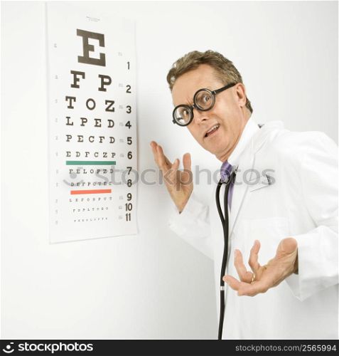 Mid-adult Caucasian male doctor wearing eyeglasses making gesture with eye chart in background.