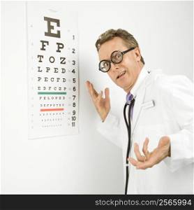 Mid-adult Caucasian male doctor wearing eyeglasses making gesture with eye chart in background.