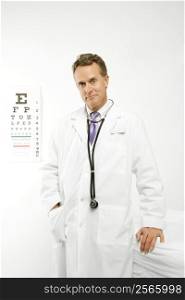 Mid-adult Caucasian male doctor with eye chart in background.