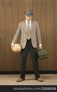 Mid-adult Caucasian male holding a globe and carrying luggage.
