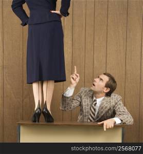 Mid-adult Caucasian male pointing up to Caucasian female standing on desk.