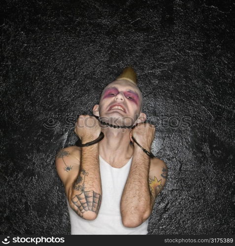 Mid-adult Caucasian male punk holding handcuffs beneath chin.