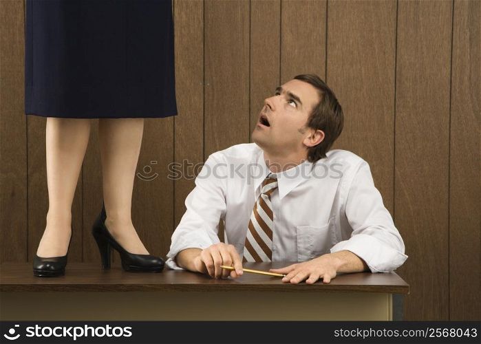 Mid-adult Caucasian male sitting at desk looking up to Caucasian female standing on desk.