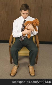 Mid-adult Caucasian male sitting in chair holding a stuffed animal looking sad.