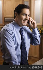 Mid-adult Caucasian male smiling and holding cell phone while standing in kitchen.