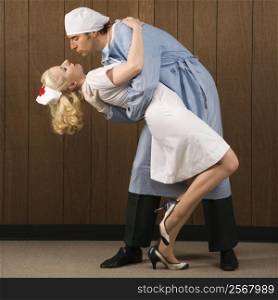 Mid-adult Caucasian male surgeon bending female nurse over backwards for passionate embrace.