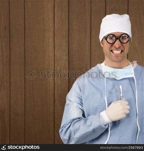 Mid-adult Caucasian male surgeon wearing thick glasses and holding scalpel smiling maniacally.