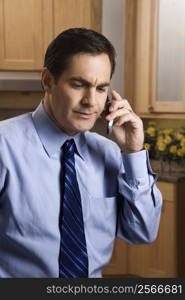 Mid-adult Caucasian male with a serious expression holding a cell phone while standing in kitchen.