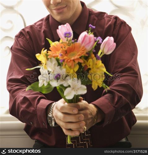 Mid adult Caucasian man holding bouquet of flowers at viewer.