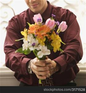 Mid adult Caucasian man holding bouquet of flowers at viewer.