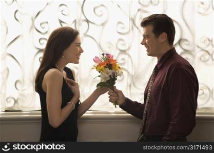 Mid adult Caucasian man presenting surprised woman with bouquet of flowers.
