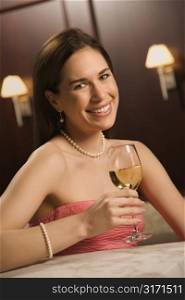 Mid adult Caucasian woman sitting at bar drinking glass of white wine and smiling.