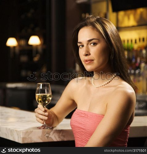 Mid adult Caucasian woman sitting at bar with glass of white wine looking at viewer.
