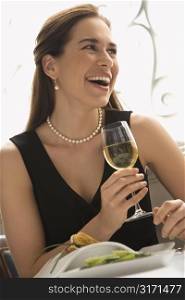 Mid adult Caucasian woman smiling and drinking white wine in restaurant.