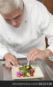 Mid- adult chef arranges edible flowers on salad