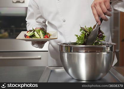 Mid- adult chef lifts leaf vegetables onto side plate