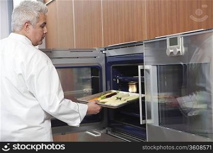 Mid- adult chef places baking tray in oven