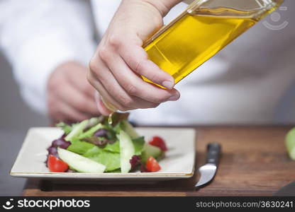 Mid- adult chef pours olive oil over side salad