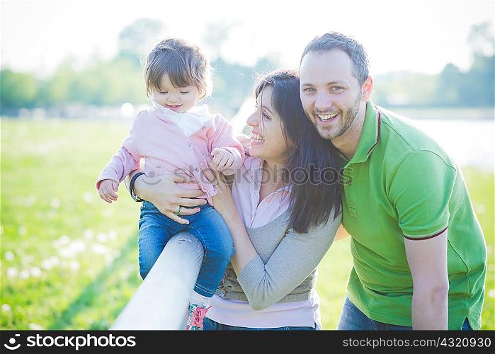 Mid adult couple and toddler daughter sitting on fence in park