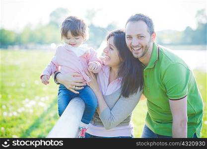 Mid adult couple and toddler daughter sitting on fence in park