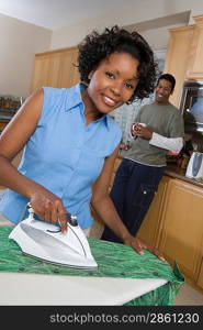 Mid-adult couple at domestic kitchen, woman ironing