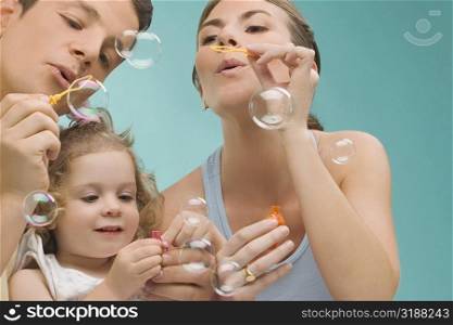 Mid adult couple blowing bubbles with their daughter