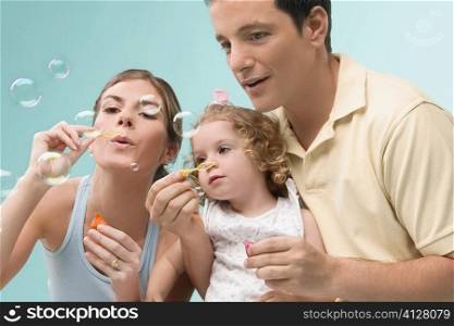 Mid adult couple blowing bubbles with their daughter