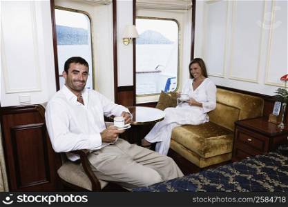 Mid adult couple drinking tea in a cabin of a sailing ship and smiling