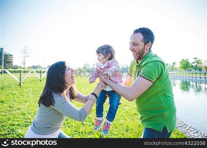 Mid adult couple handing toddler daughter to each other in park