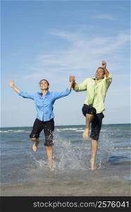 Mid adult couple jumping with holding each other hands on the beach