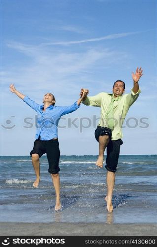 Mid adult couple jumping with holding each other hands on the beach