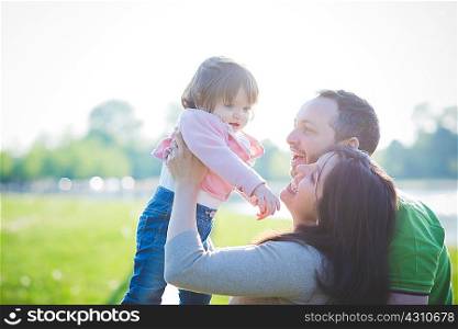Mid adult couple lifting up toddler daughter in park