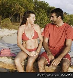 Mid adult couple looking at each other and sitting on a jetty
