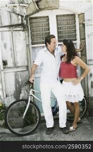 Mid adult couple looking at each other with a bicycle in front of a house