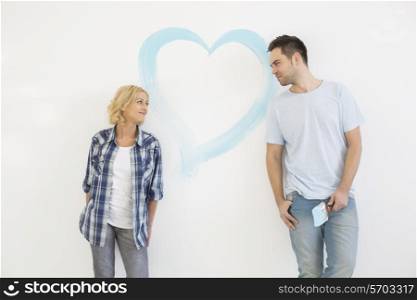 Mid-adult couple looking at each other with painted heart on wall