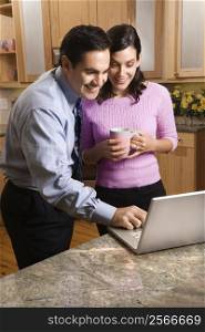 MId-adult couple looking at laptop computer while drinking coffee in kitchen.