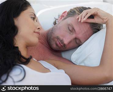 Mid-adult couple lying in bed, woman touching men&acute;s forehead