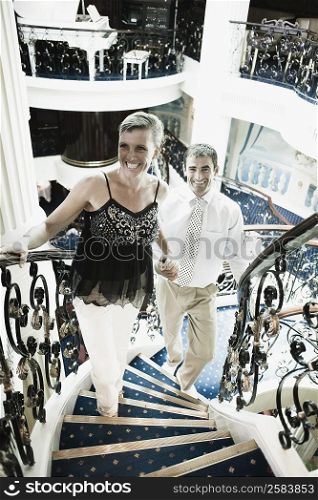 Mid adult couple moving up on a staircase of a cruise ship and smiling