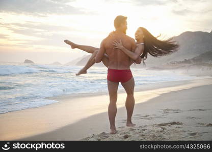 Mid adult couple on beach,man carrying woman in arms, rear view