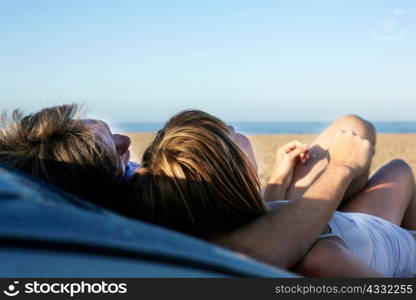 Mid adult couple relaxing on car on beach