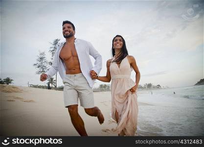 Mid adult couple running along beach, hand in hand, low angle view