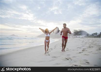 Mid adult couple running along beach in swimwear