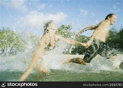 Mid adult couple running in water on the beach