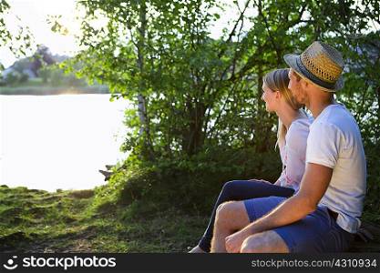 Mid adult couple sitting by lake watching sunset