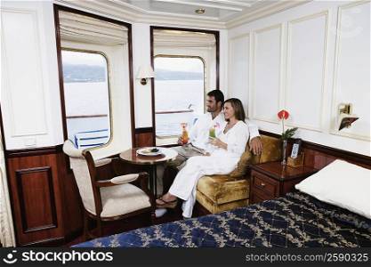 Mid adult couple sitting in a cabin of a sailing ship and holding glasses of cocktail and smiling