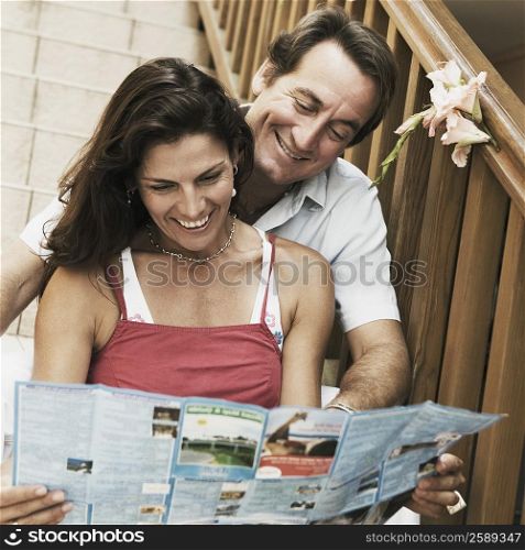 Mid adult couple sitting on a staircase and looking at a brochure and smiling