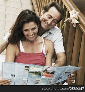 Mid adult couple sitting on a staircase and looking at a brochure and smiling